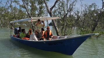Ein Boot mit mehreren Personen, die Rettungswesten tragen, fährt durch ein Mangrovengebiet.