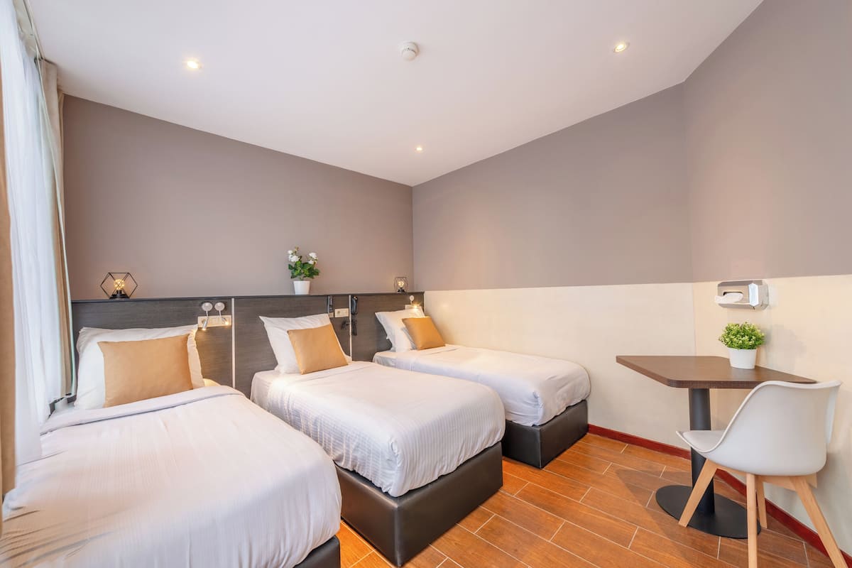 A hotel room with three beds, a small table, and a chair.