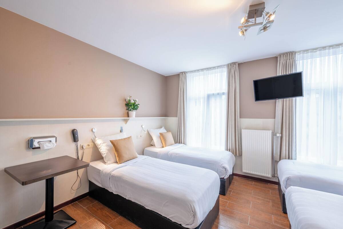 A hotel room with two beds, a flat-screen TV, a bedside table, a telephone, and a radiator.