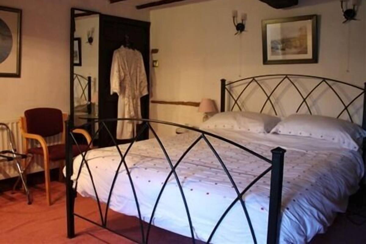 A bedroom with a metal bed frame, a chair, a radiator, and a door leading to another room.