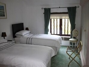 A room with two single beds, a window with curtains, a chair, and a painting on the wall. - Church Villa B&B (Chesterfield)
