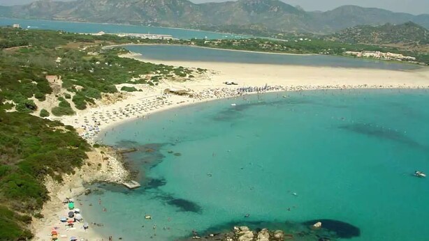 A coastal area with a sandy beach, clear turquoise waters, and a mountainous backdrop. - Residence la Chimera (Villasimius)