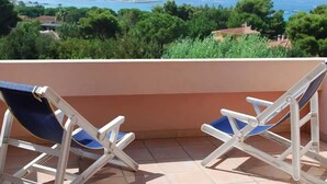 A balcony with two folding chairs facing a scenic view of the sea and greenery. - Residence la Chimera (Villasimius)
