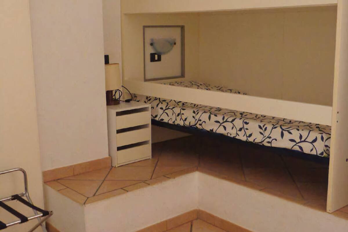 A small, compact room with a bunk bed, a desk with a chair, and a framed picture on the wall.