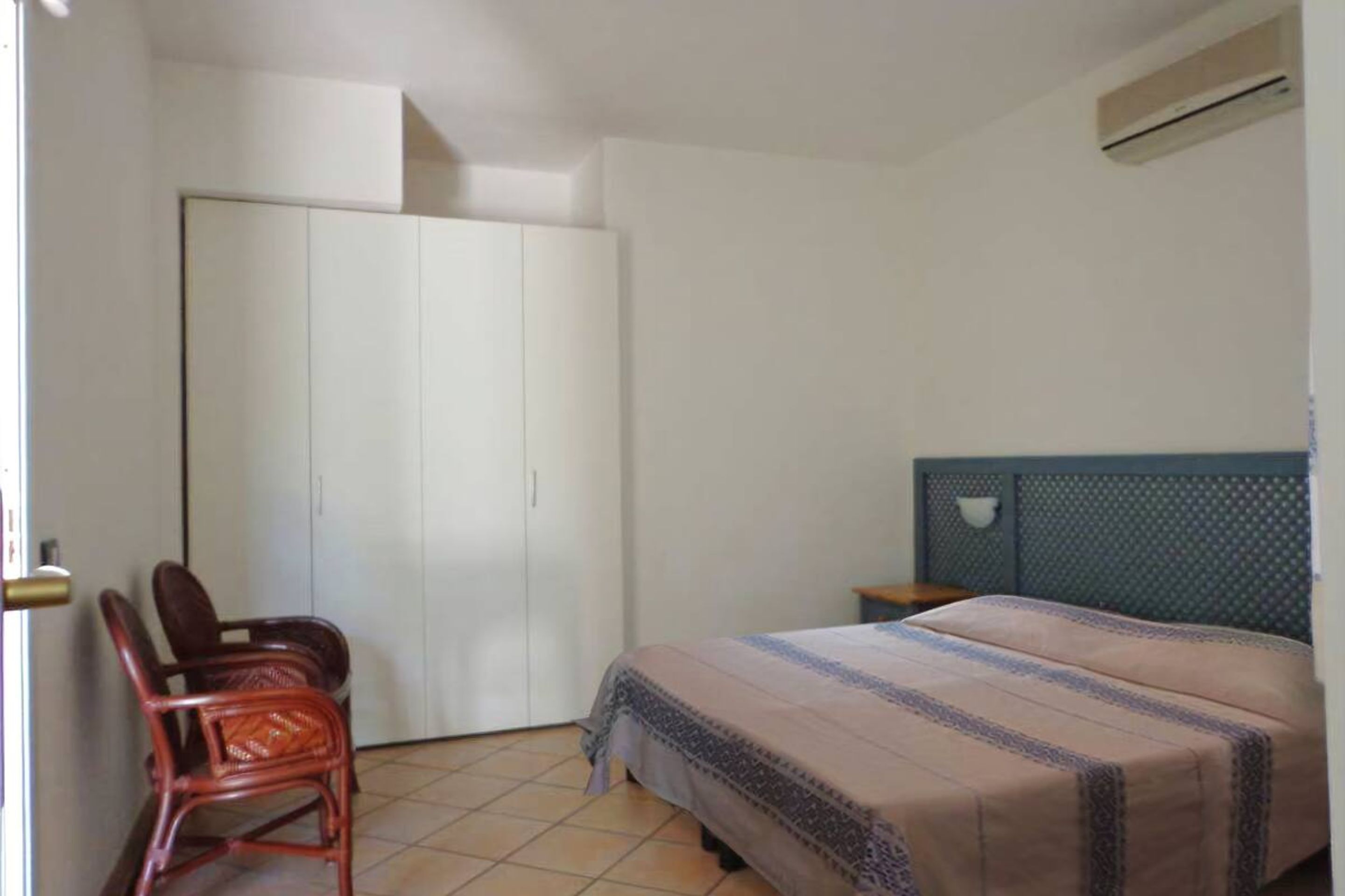 Un dormitorio con cama, armario, silla y aire acondicionado.