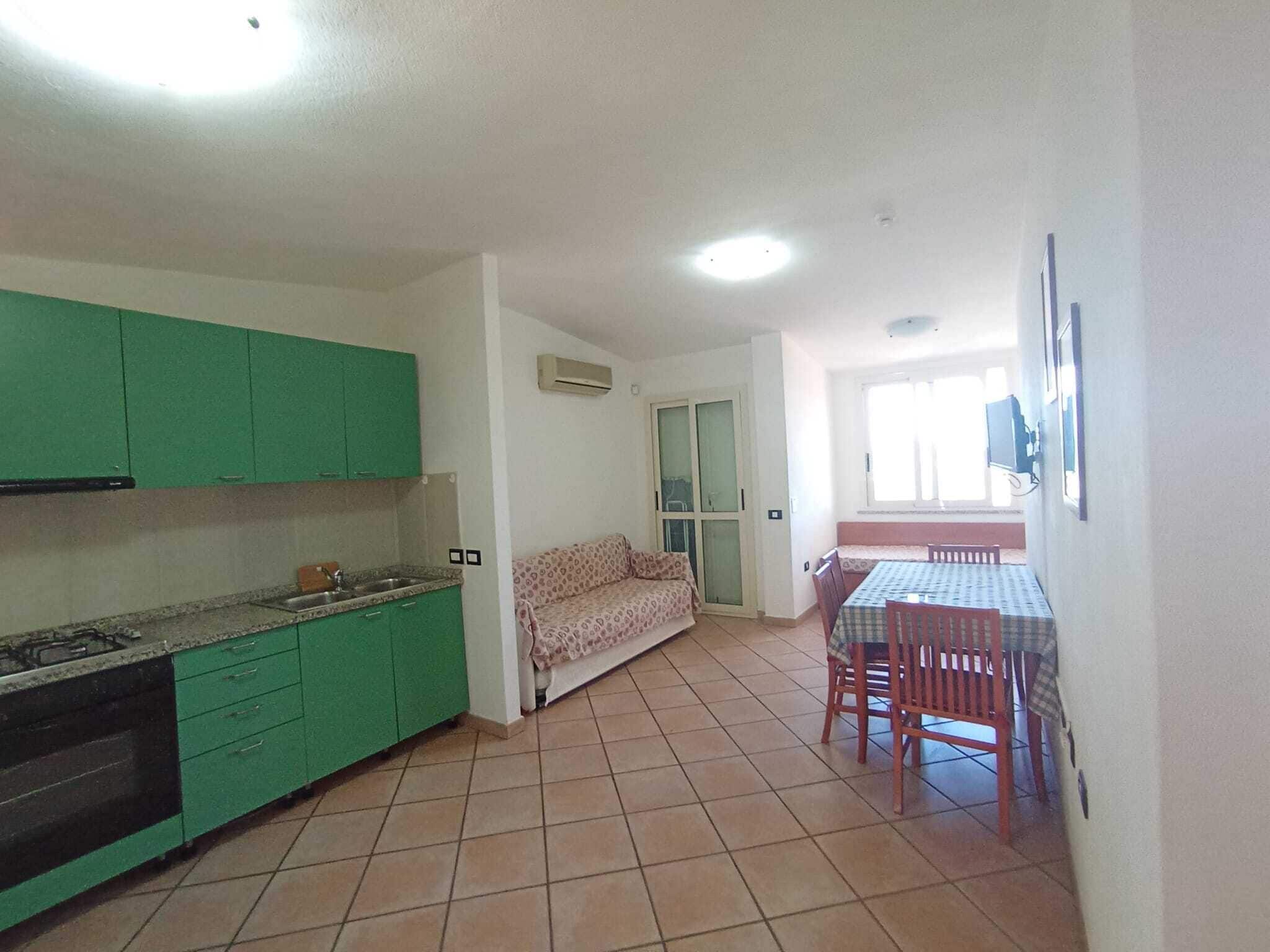 A compact kitchen with green cabinets, a dining area with a table and chairs, and a sofa.