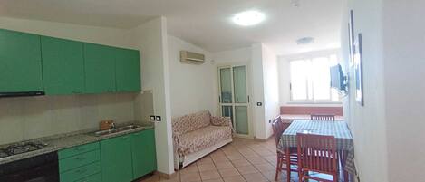 A compact kitchen with green cabinets, a dining area with a table and chairs, and a sofa.