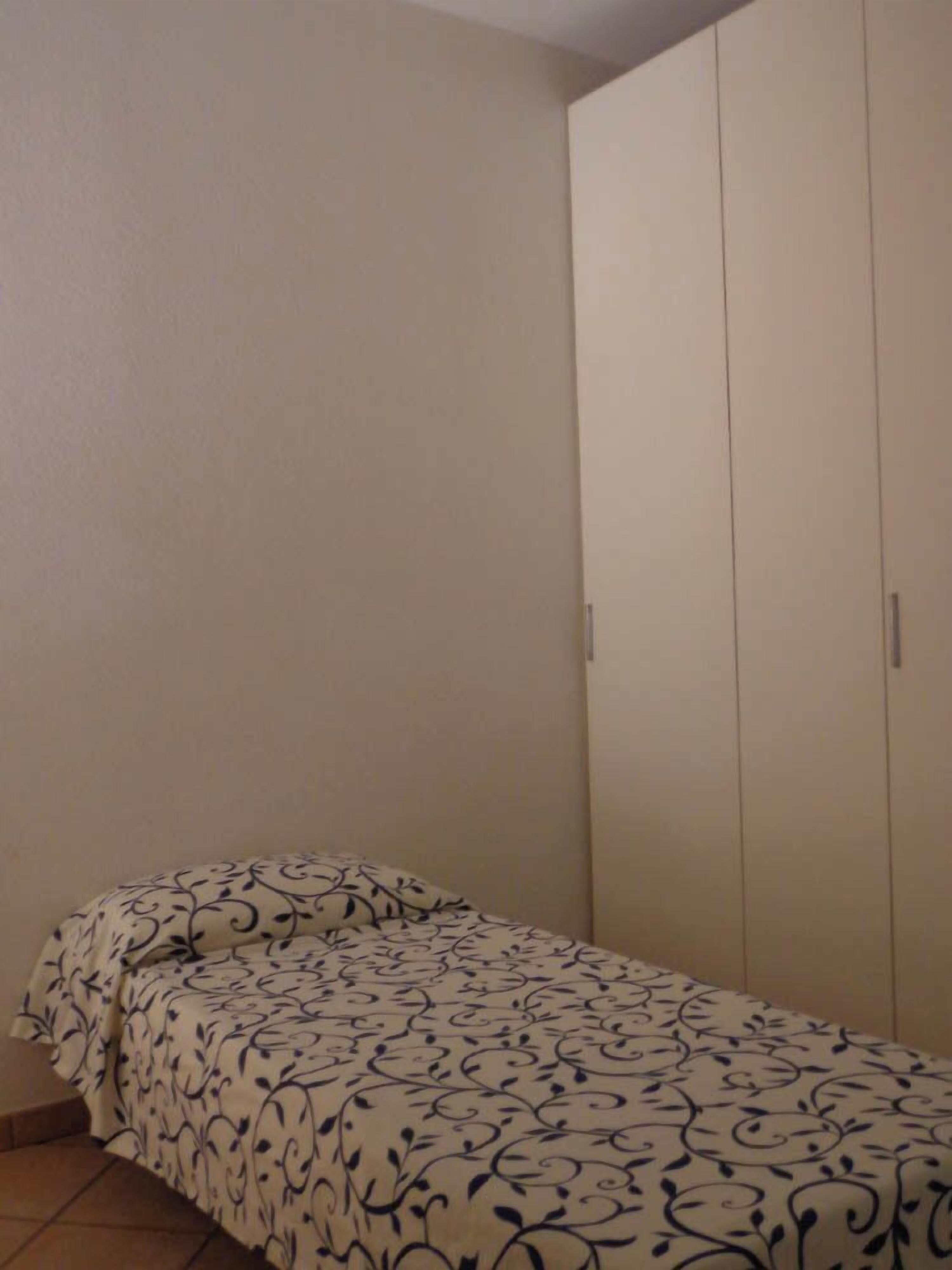 A small bedroom with a bed, a wardrobe, and a tiled floor.