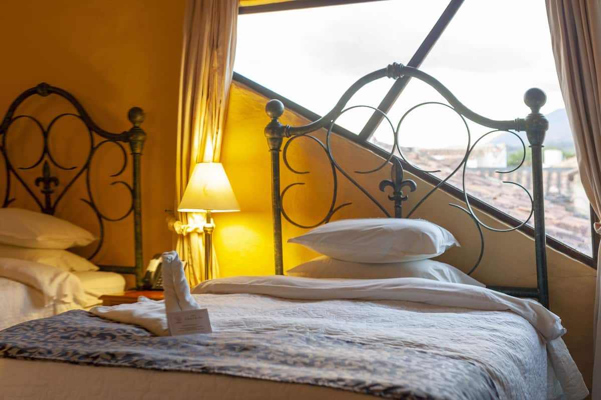 Een hotelkamer met twee bedden, een raam met gordijnen, een bedlampje en een ingelijste foto aan de muur.