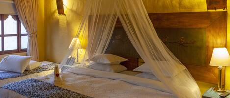 Une chambre avec un lit sous un dais, deux tables de chevet avec des lampes et un tableau au mur.