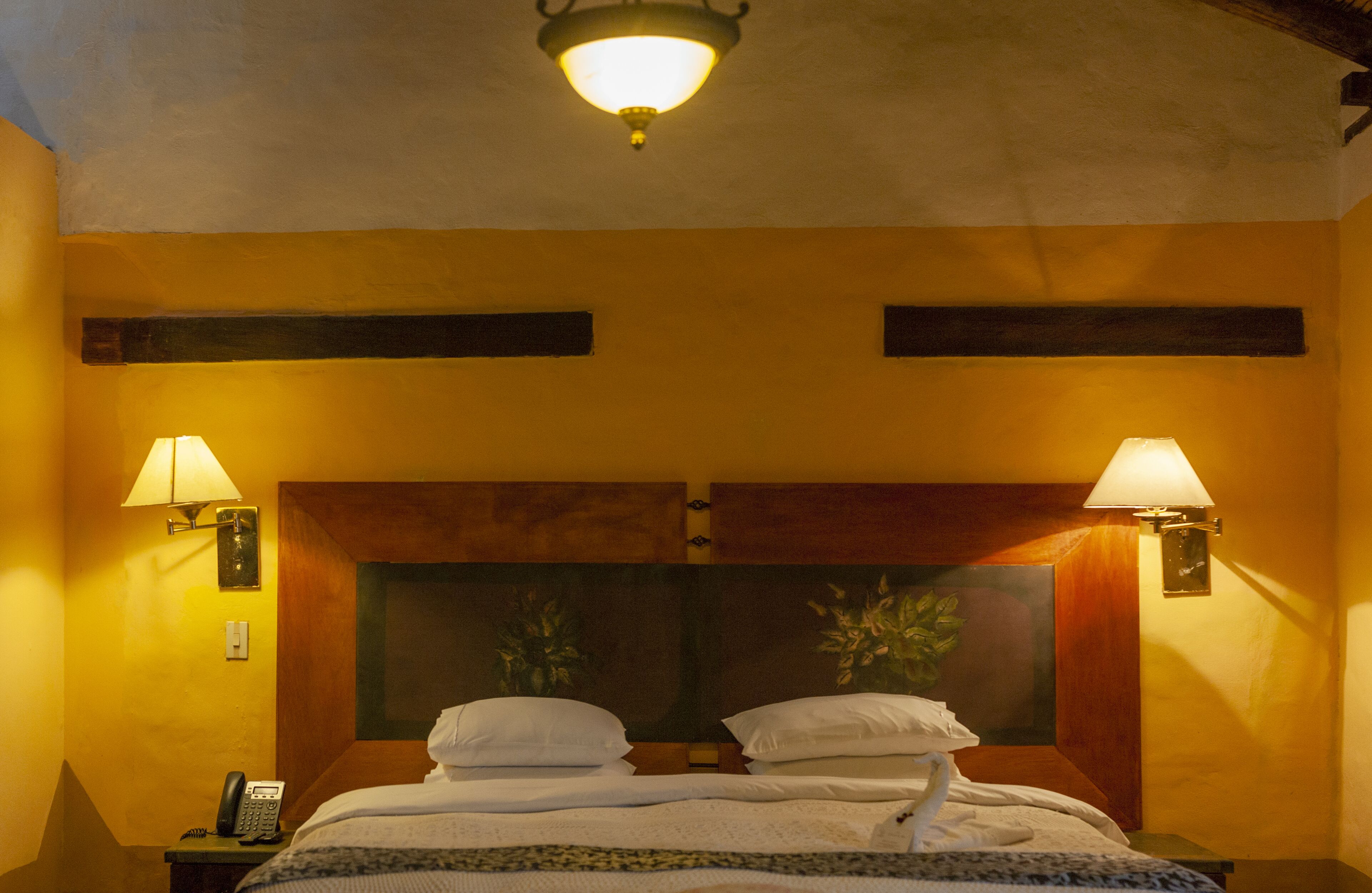 Une chambre d’hôtel équipée d’un lit, de deux lampes fixées au mur, d’un téléphone et d’un luminaire au plafond.