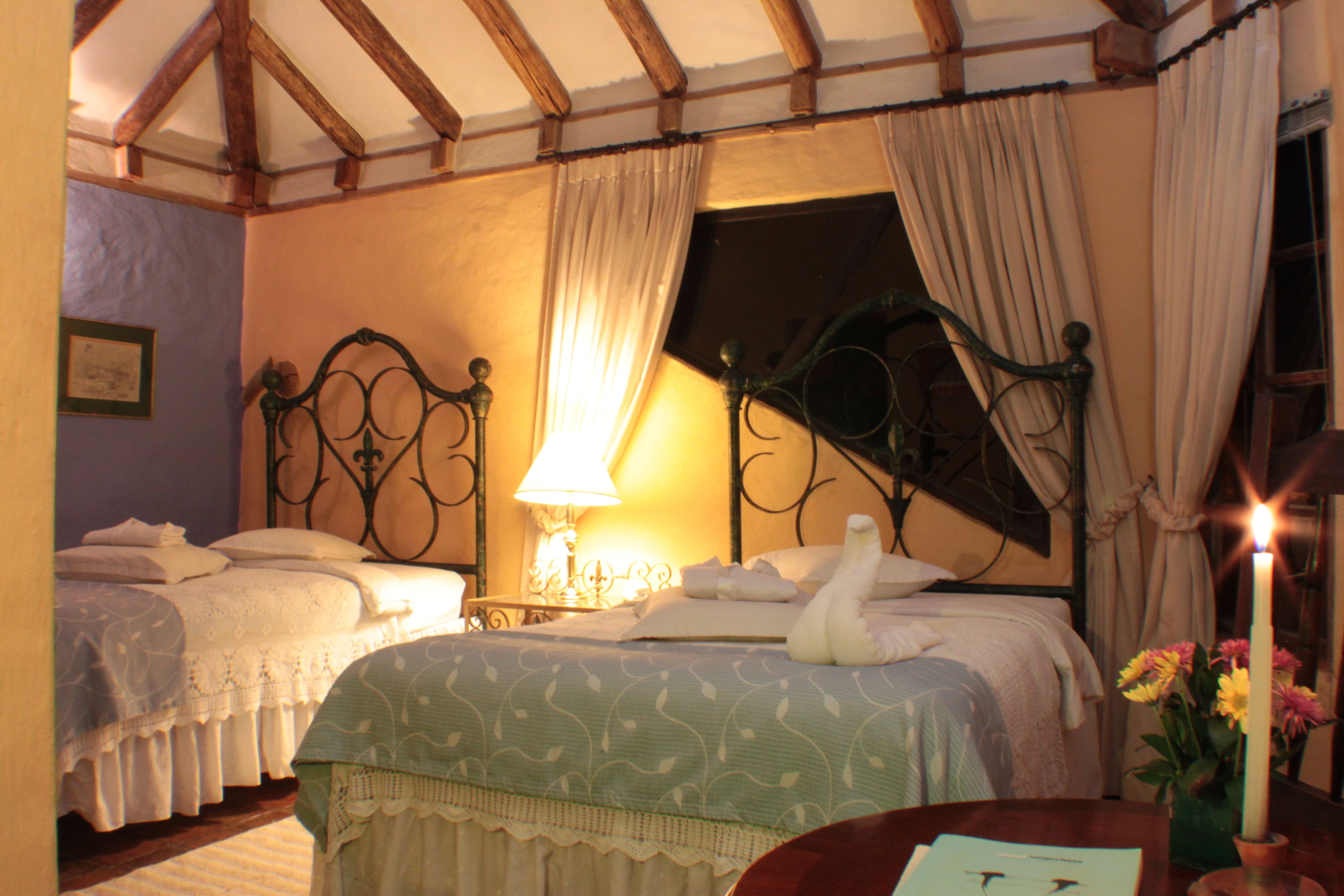 A bedroom with two beds, a nightstand with a lamp, a vase with flowers, and a candle on the table.
