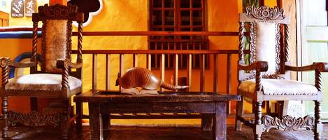 A room with two ornate wooden chairs, a wooden bench, and a large shell on the bench.