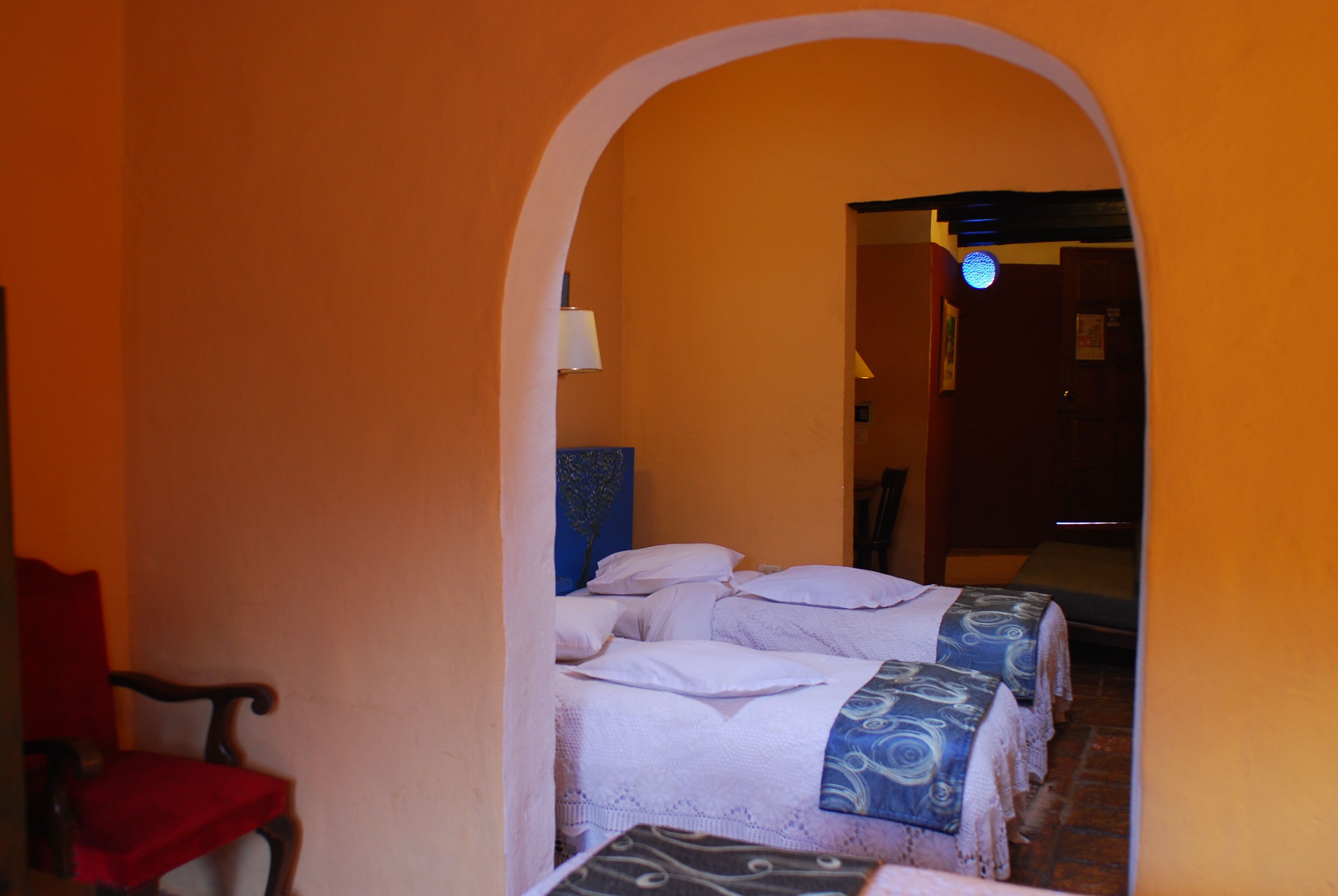 A corridor with a bed at the end, a red chair, and a lamp.