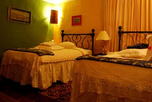 Una habitación con dos camas, cada una con una colcha blanca y un cabecero decorativo. Hay dos lámparas de pared y un cuadro enmarcado en la pared.