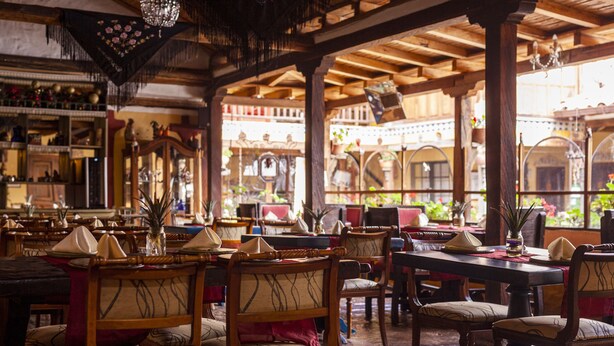 A restaurant with wooden tables and chairs, large windows, and a chandelier.