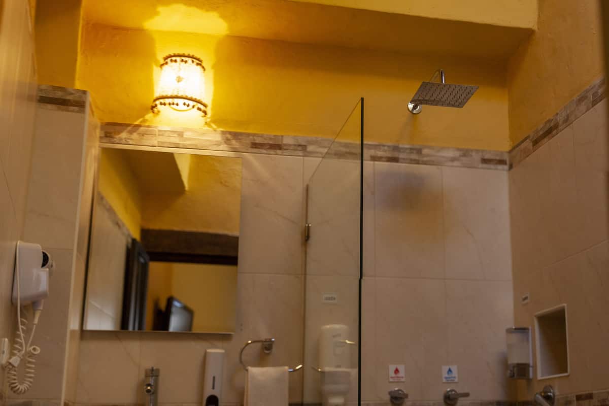 Een badkamer met een glazen douchecabine, een wastafel met spiegel, een handdoekhouder en een handdroger.