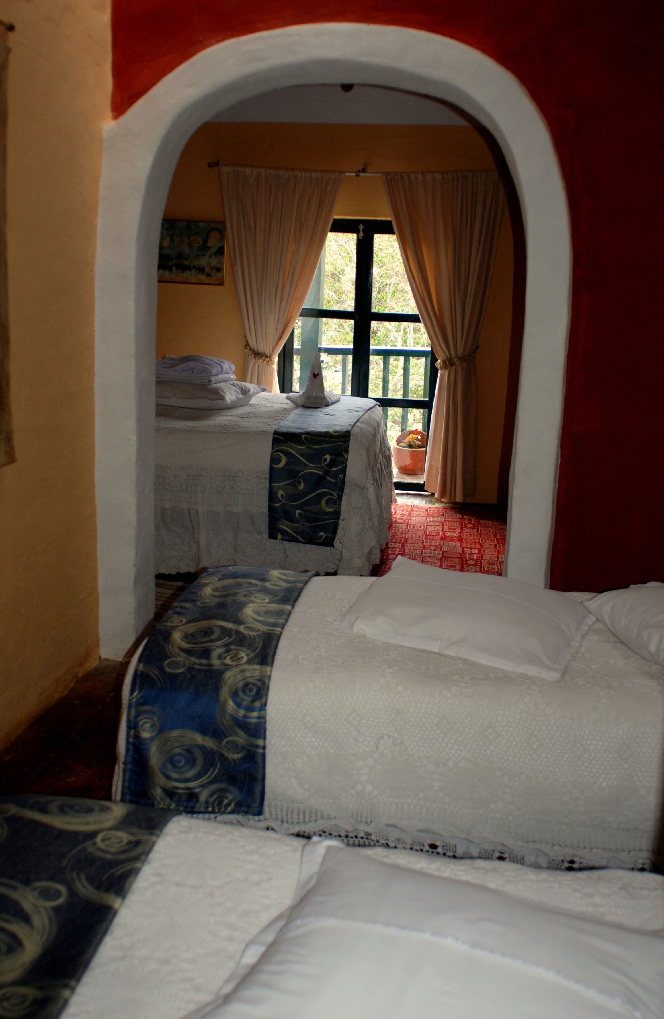 A narrow hallway leading to a bedroom with two beds, one with a blue patterned bedspread and the other with a white bedspread.