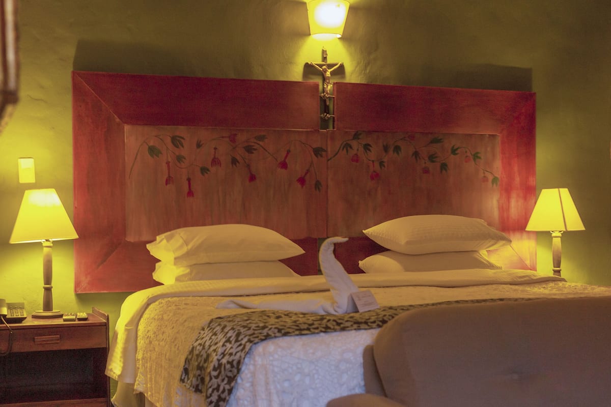 Een hotelkamer met een bed, twee bedlampen, een houten hoofdeinde met bloemistisch kunstwerk en een houten deur.