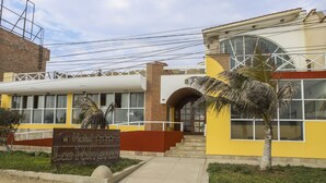 Um hotel com fachada amarela, uma placa de identificação e uma palmeira em primeiro plano.