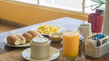 Desayuno con panecillos, huevos revueltos, un vaso de zumo de naranja y una taza de café sobre una mesa con un menú.