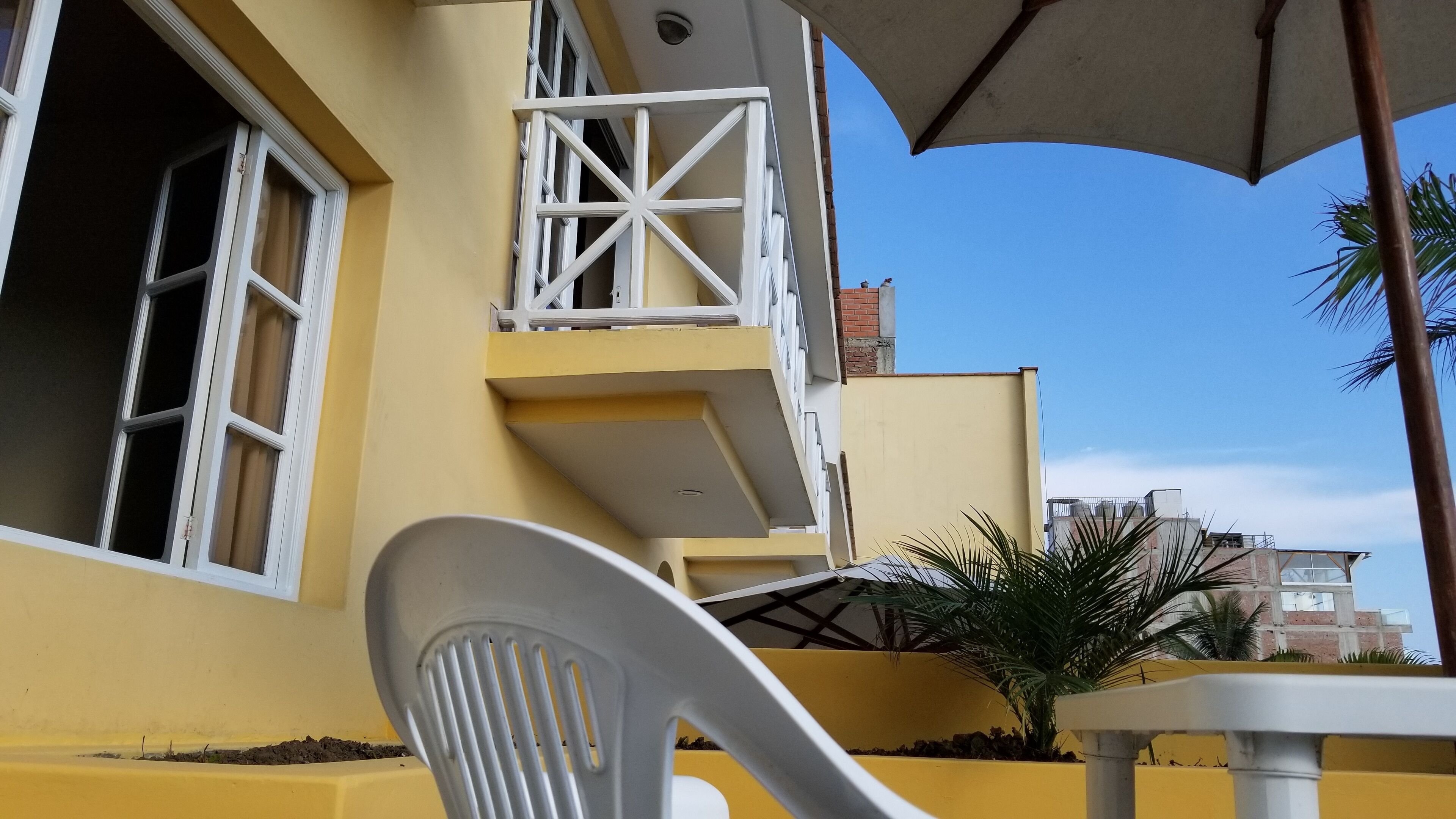 A yellow building with white balconies, a white chair, and a table under a large umbrella.