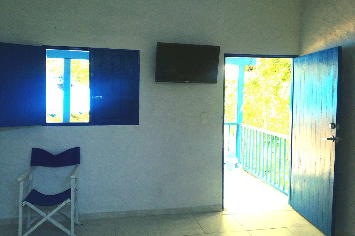 Una habitación con una puerta azul, una ventana, una silla y un televisor de pantalla plana montado en la pared.