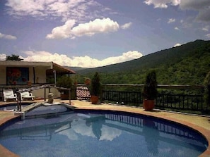 A pool area with lounge chairs, a small building with artwork, and a mountainous backdrop.