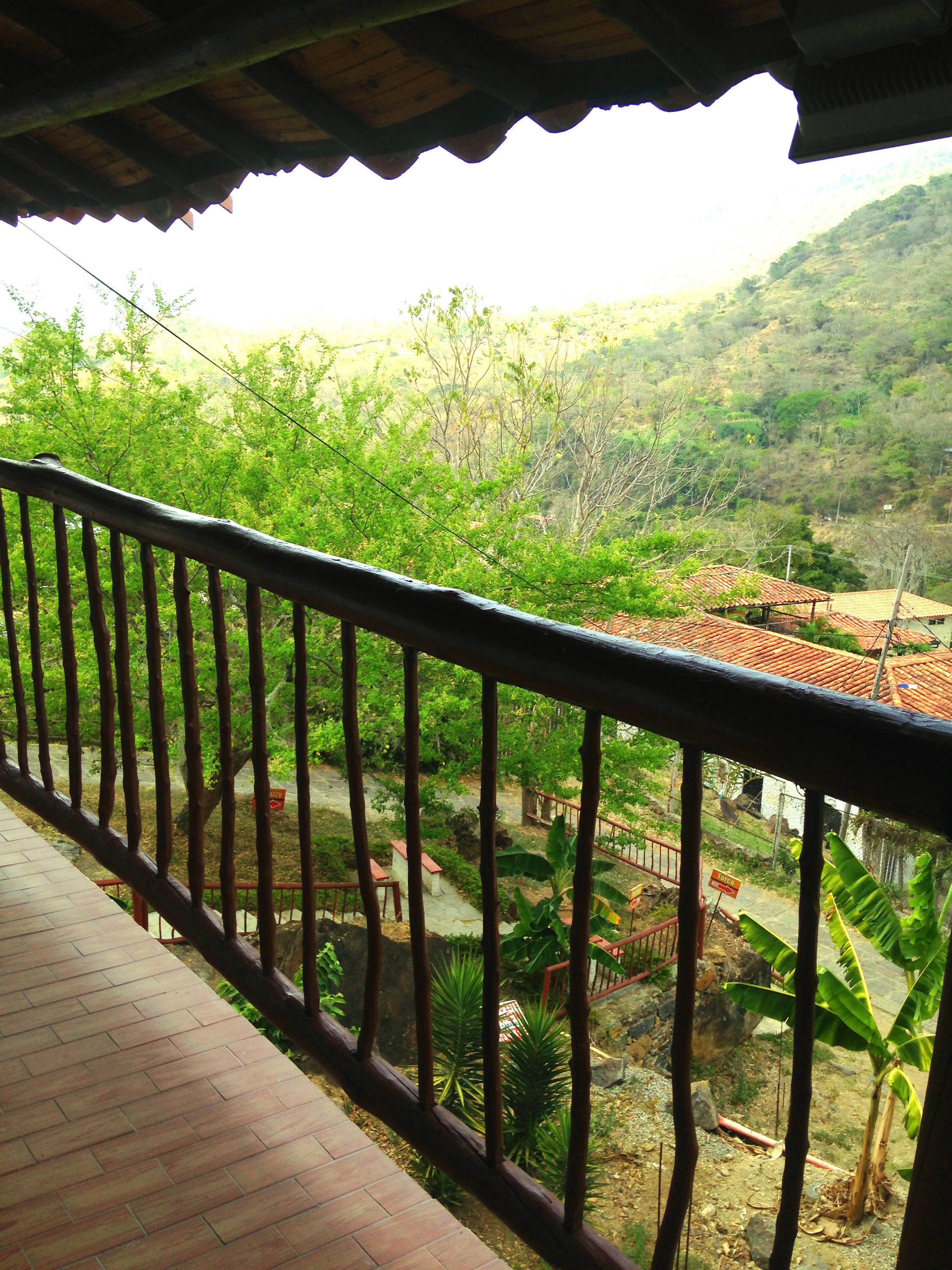 Un balcón con vistas a un paisaje rural, que incluye árboles y un pueblo distante.