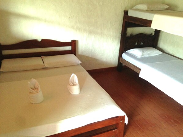 Una habitación con dos camas, una con cabecera de madera y la otra tipo litera. Hay almohadas y toallas sobre las camas.