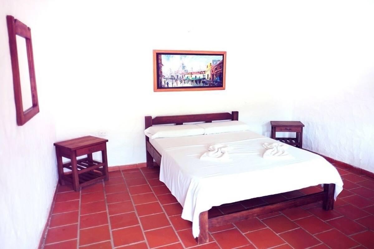 Una habitación sencilla con una cama, una mesita pequeña y un cuadro en la pared.