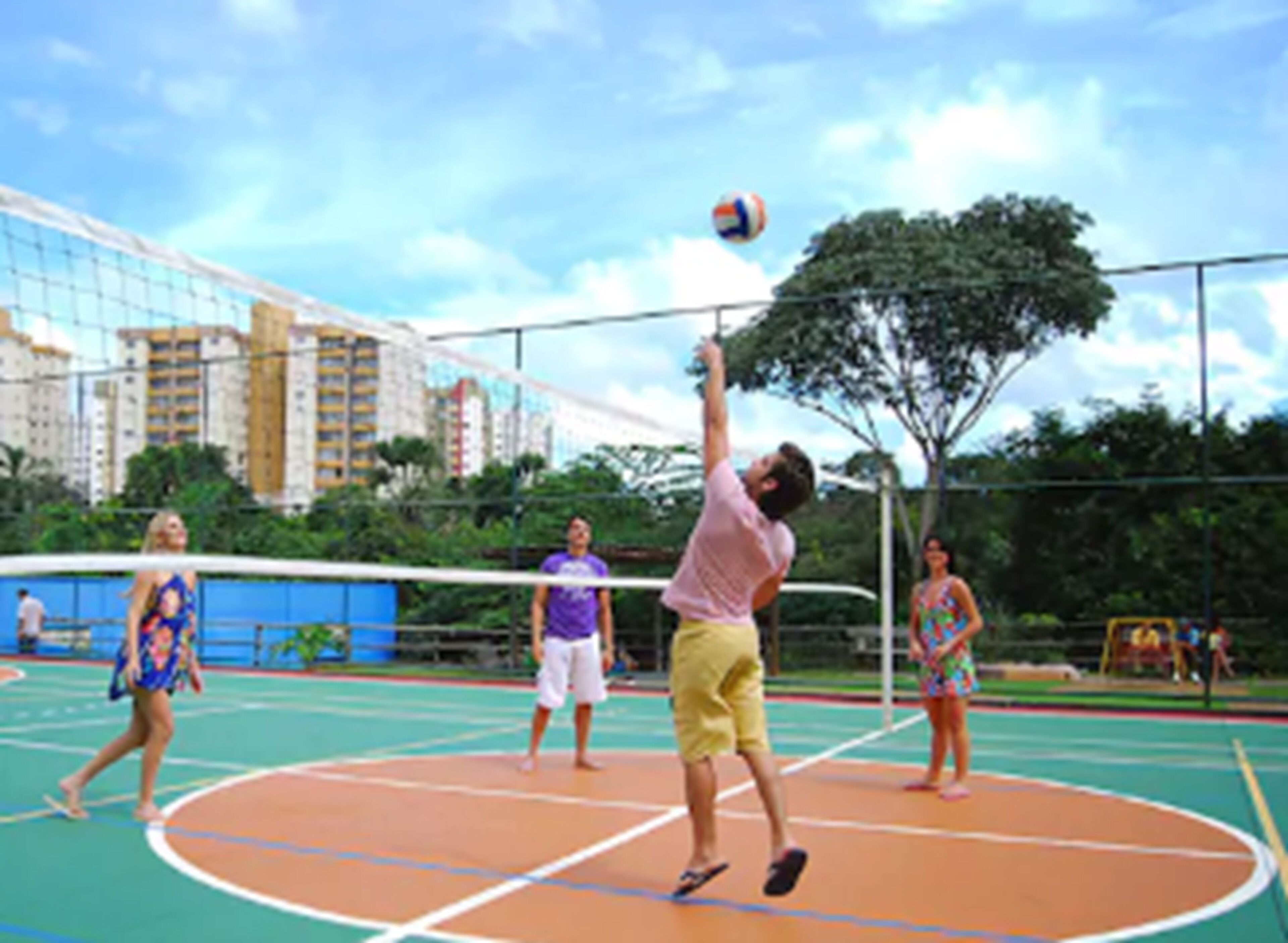 A volleyball court with a net, surrounded by greenery and buildings in the background.
