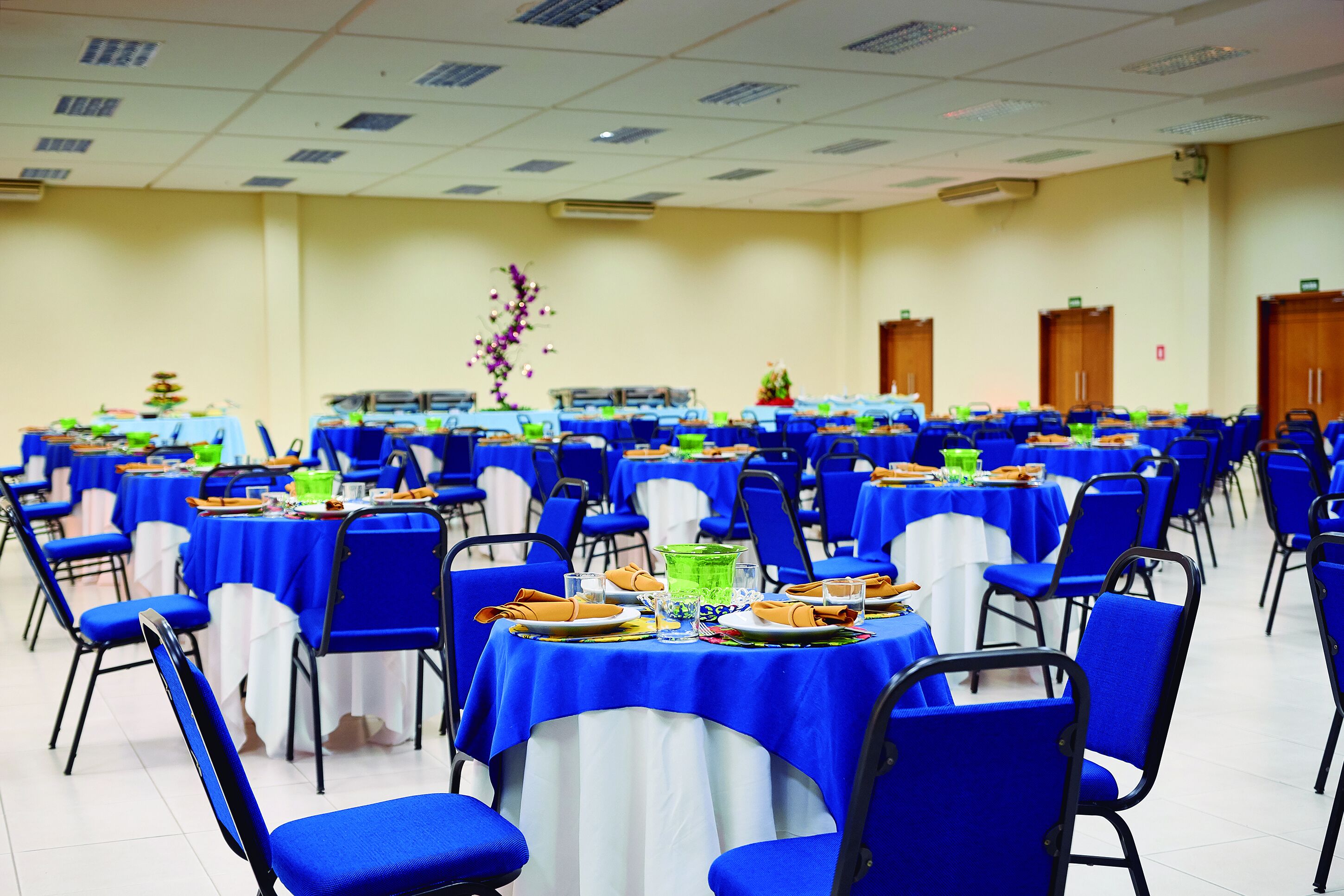 Una sala da banchetti con file di tavoli ricoperti da tovaglie blu e sedie dello stesso colore.