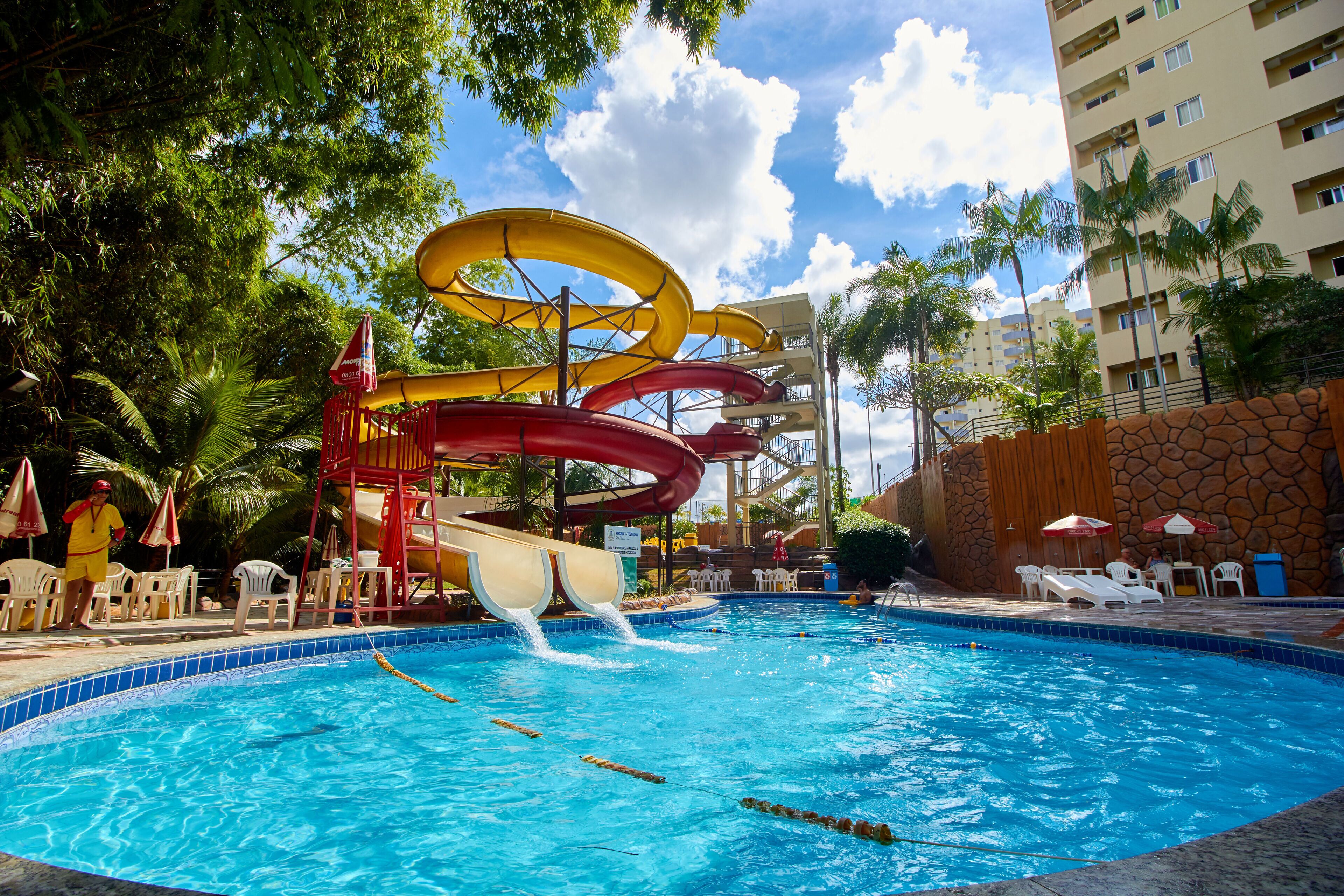 A swimming pool with multiple water slides, lounge chairs, and a stone wall.