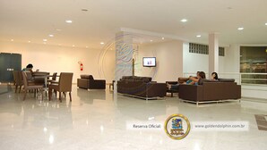 A modern lobby with a seating area, a fire extinguisher, and a television screen. - Golden Dolphin Grand Hotel OFICIAL (Caldas Novas)
