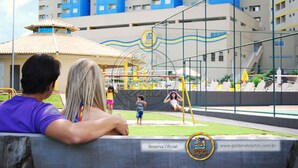 A view of a playground with children playing, a building with blue and white facades, and a website address at the bottom. - Golden Dolphin Grand Hotel OFICIAL (Caldas Novas)
