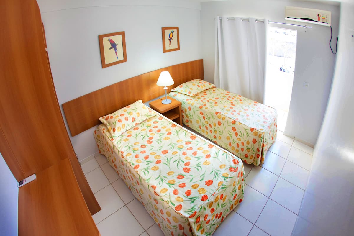 A hotel room with two beds, a nightstand, a lamp, and a window with curtains.