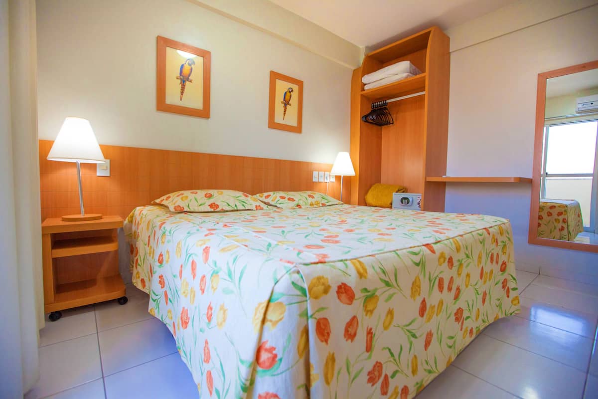 A hotel room with a bed, two wall-mounted lamps, a wooden shelf with towels, and a mirror.
