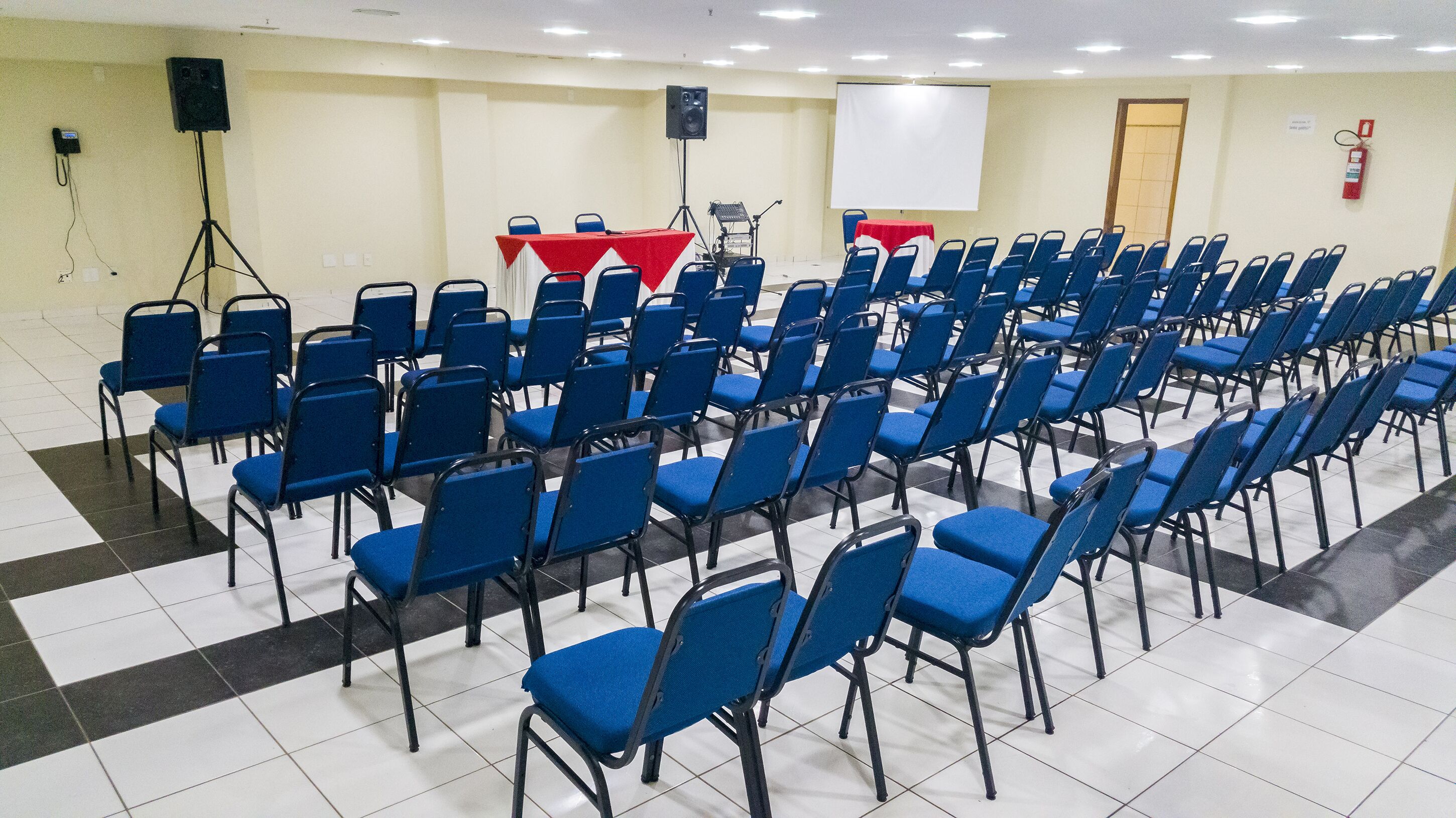 A conference room with rows of blue chairs, a whiteboard, and a red table.