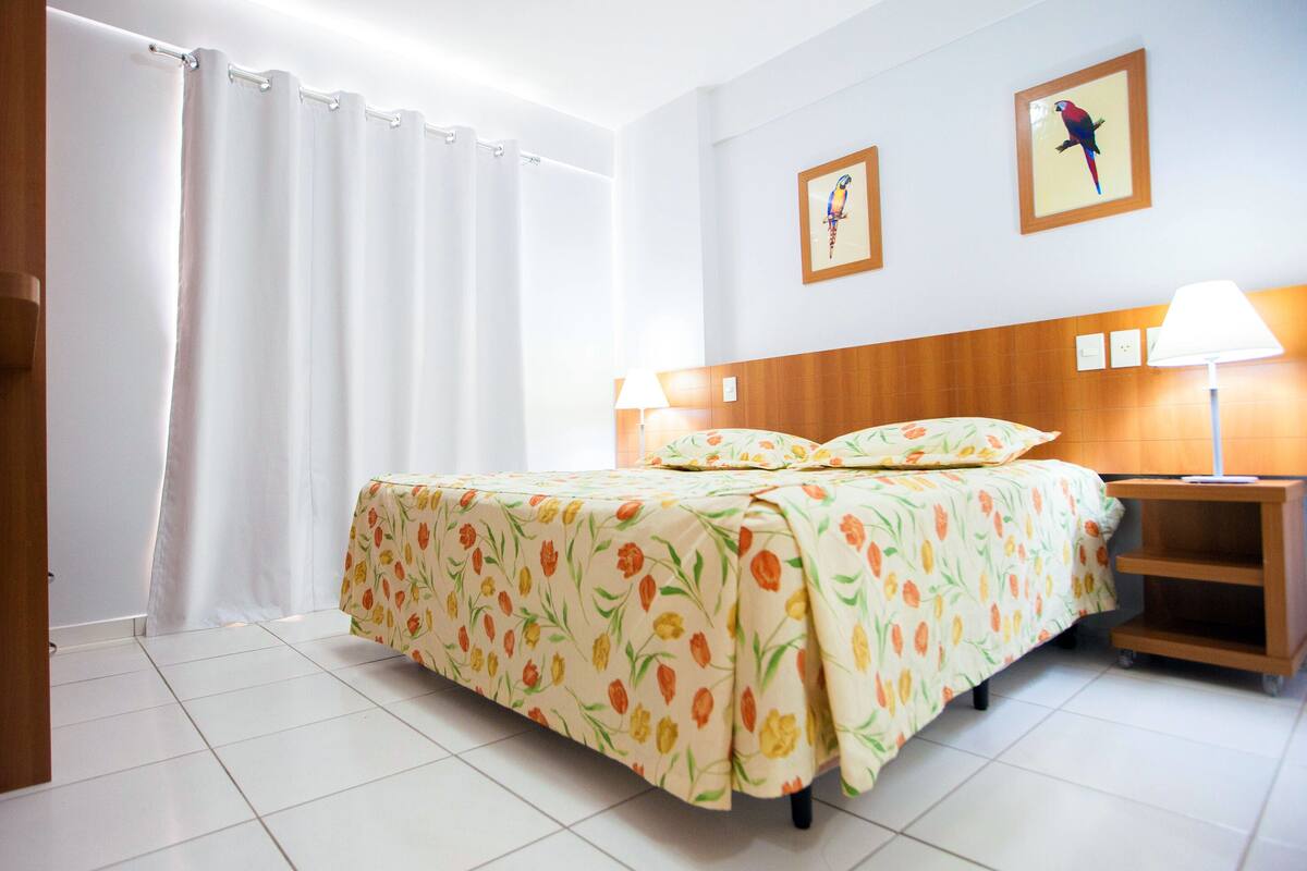 A hotel room with a bed, two nightstands, a wooden headboard, and two framed pictures on the wall.
