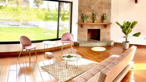 A spacious living room with a large window, a fireplace, and a modern sofa.