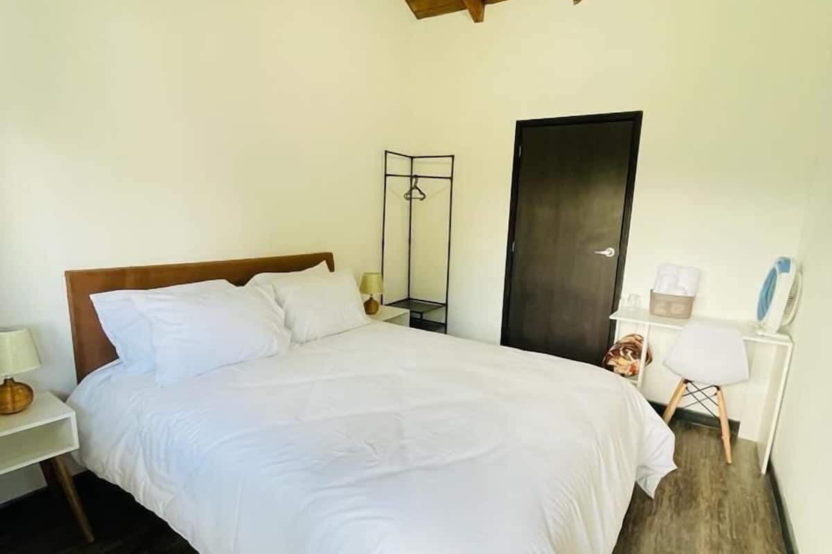 Une chambre avec un plafond en bois, un lit avec une literie blanche, une table de chevet avec une lampe, une armoire et une porte.