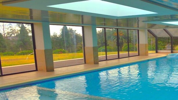 An indoor swimming pool with clear glass walls, a diving board, and a view of the outdoors.