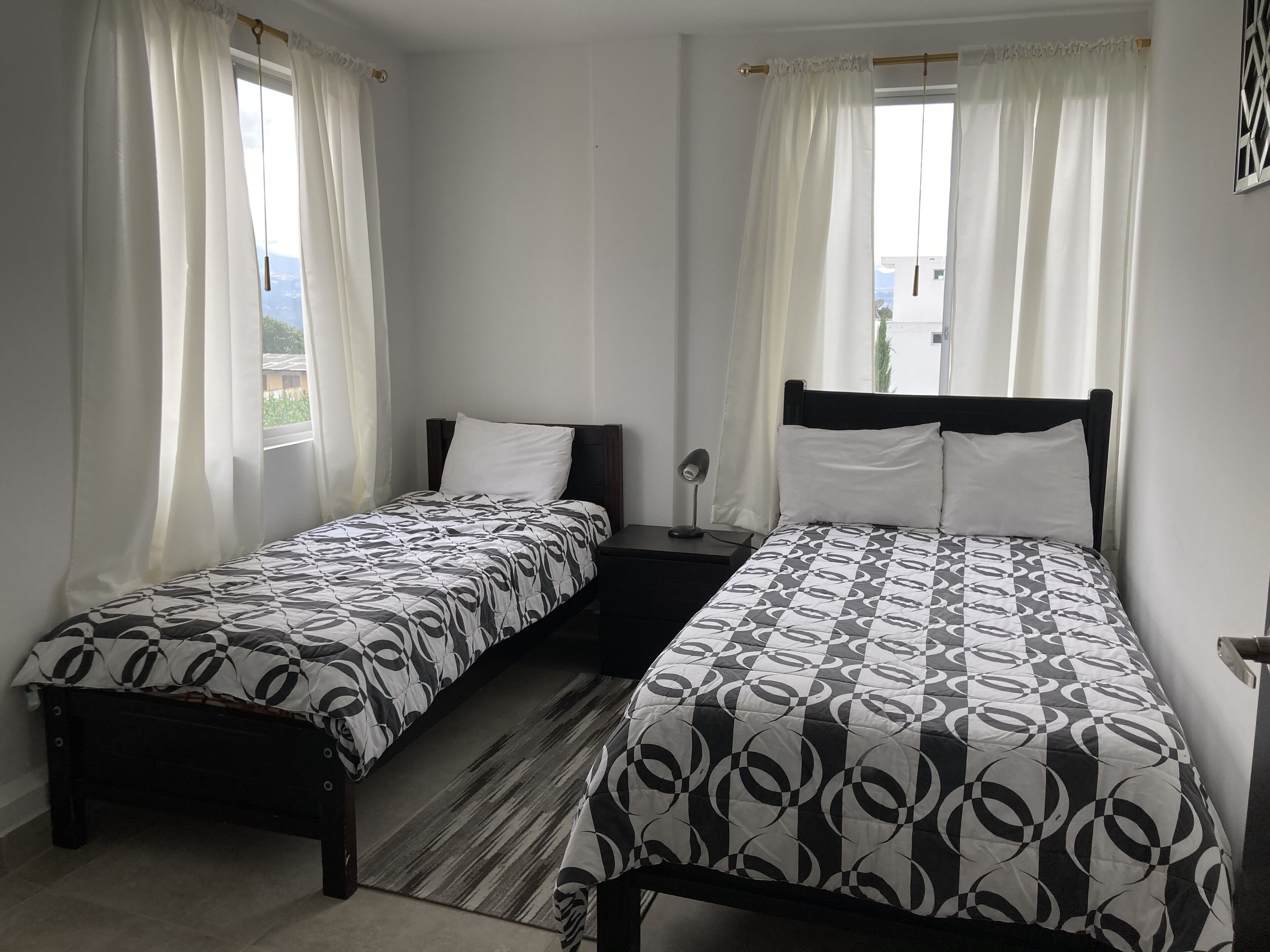 A room with two single beds, each with a patterned bedspread, a bedside table, and a lamp.