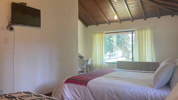 Un dormitorio con dos camas, un televisor montado en la pared, una ventana con cortinas y un techo con vigas de madera.