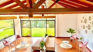 A spacious room with a wooden ceiling, large windows, a sofa, and several chairs.