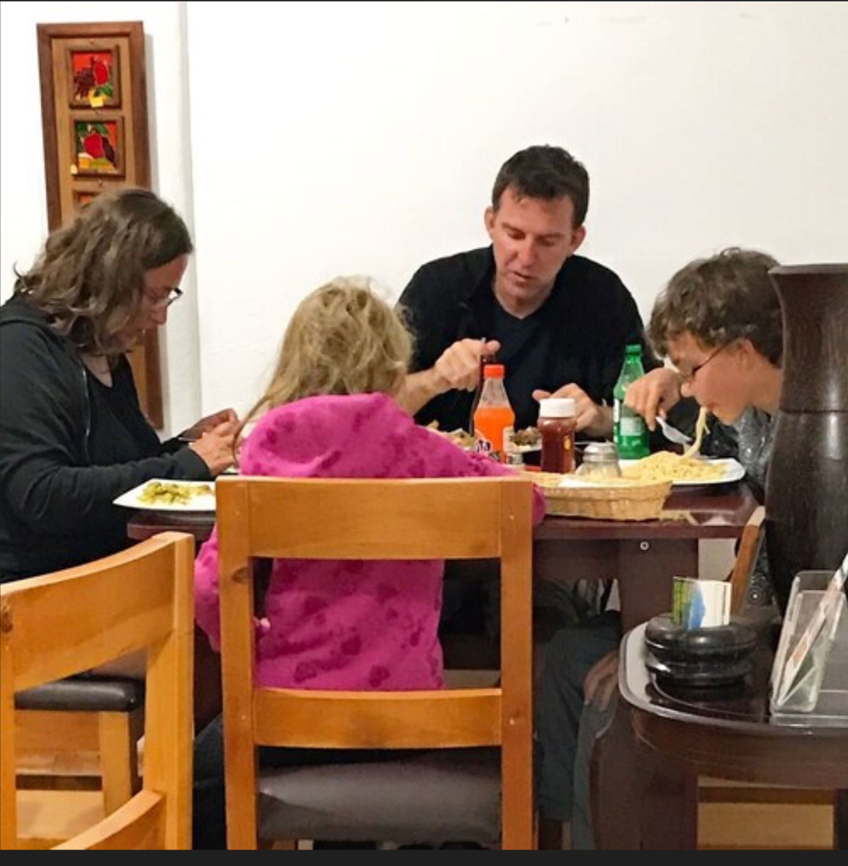 A dining table with four people seated, a bottle of orange juice, and a green bottle.