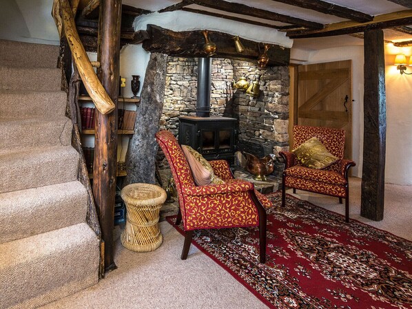 A rustic interior with a stone fireplace, wooden beams, and patterned red armchairs.