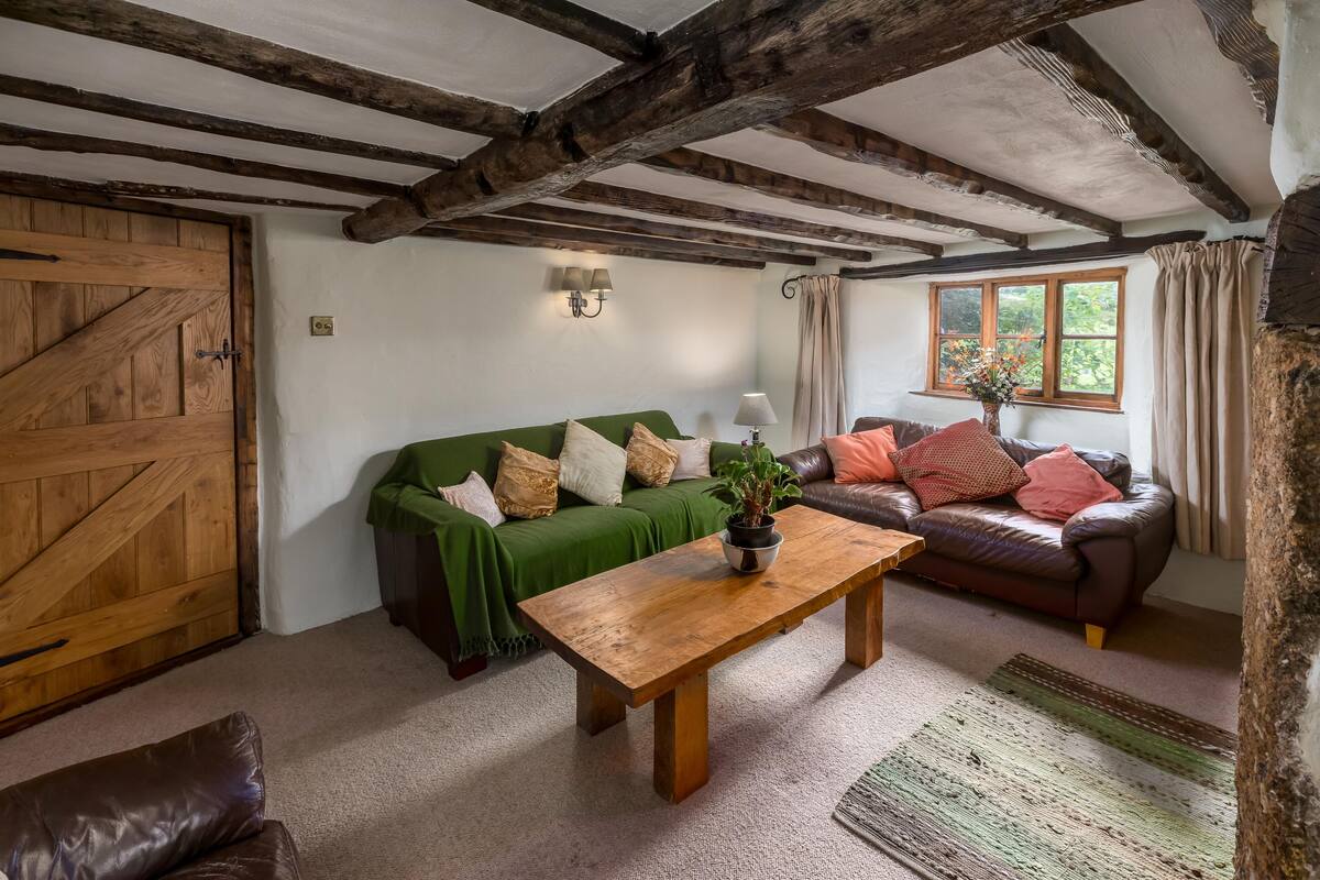 A rustic room with exposed wooden beams, a green sofa, a brown leather sofa, a wooden coffee table, and a large wooden door.
