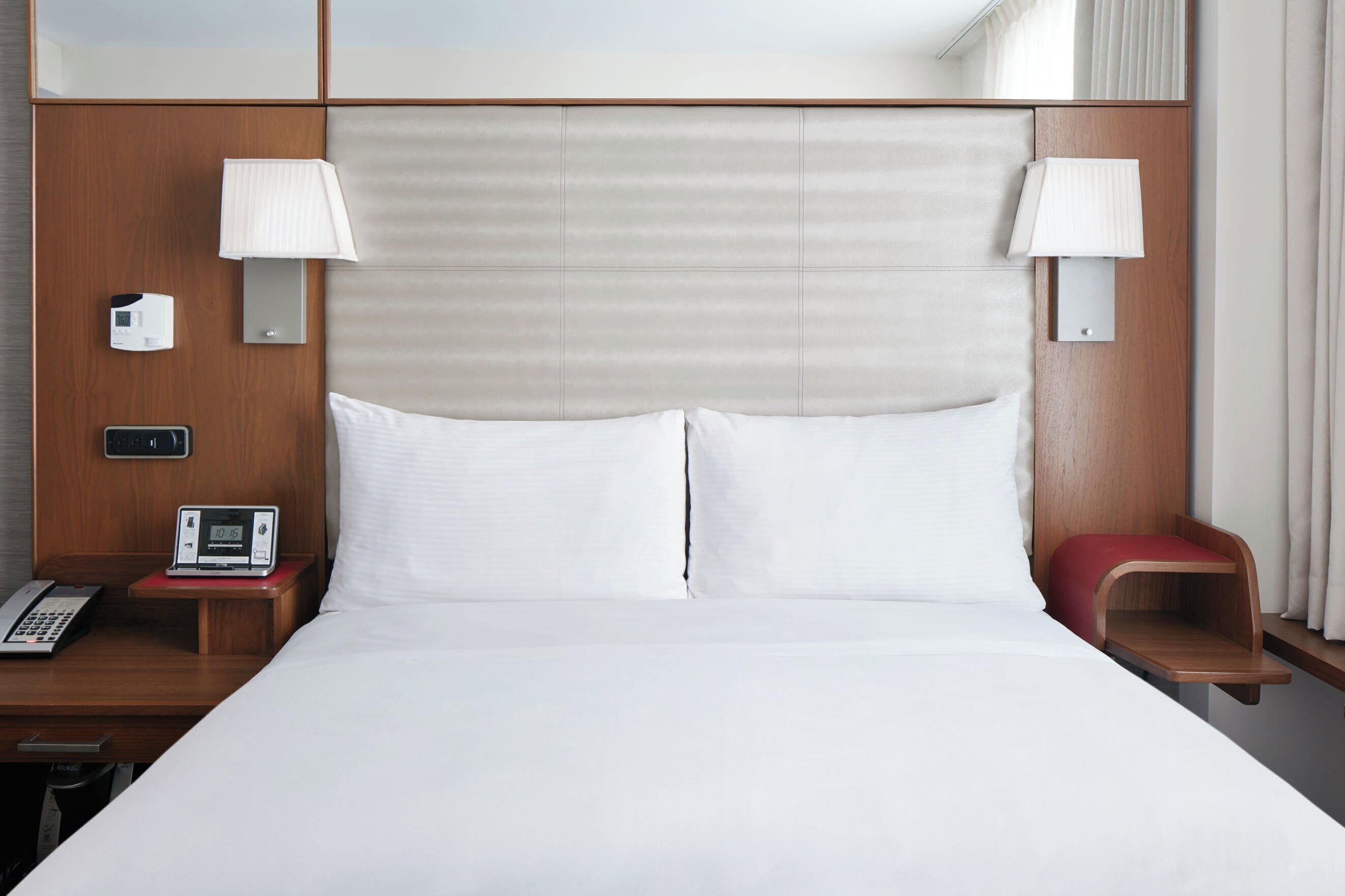 Una habitación de hotel con una cama grande, dos lámparas de noche, un teléfono junto a la cama y una mesita con una lámpara.